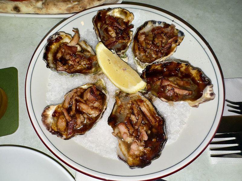 A plate of oysters Kilpatrick with a lemon wedge at a restaurant in Cairns, Queensland
